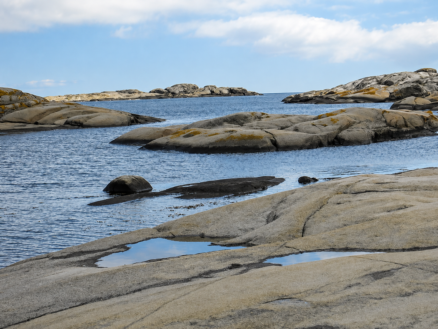 Calm blue water flowing between smooth granite rocks under a bright sky